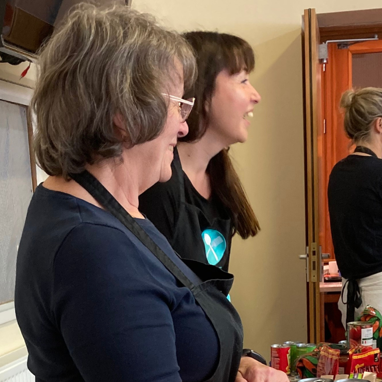 Two smiling FEAST volunteers serving tinned food