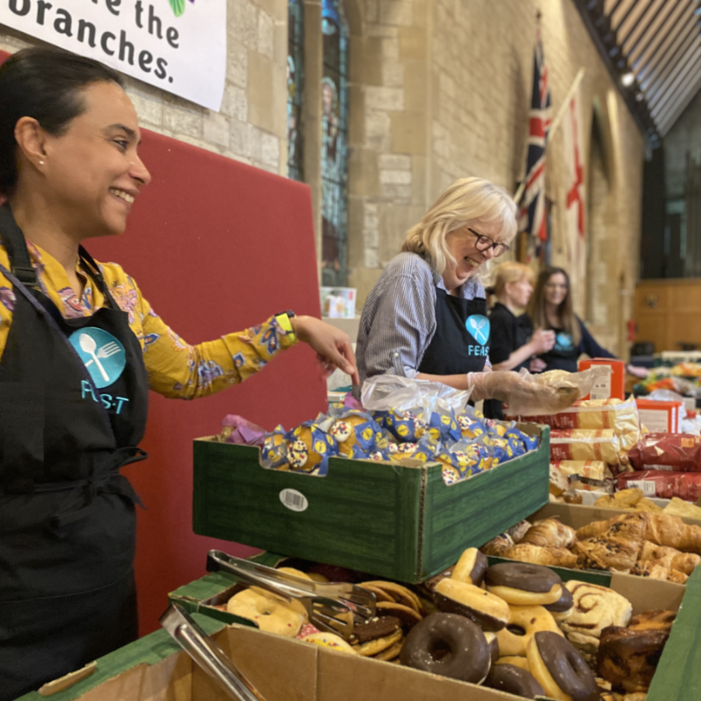 Four FEAST larder volunteers serving bread, cakes and other foodstuffs at the community larder.