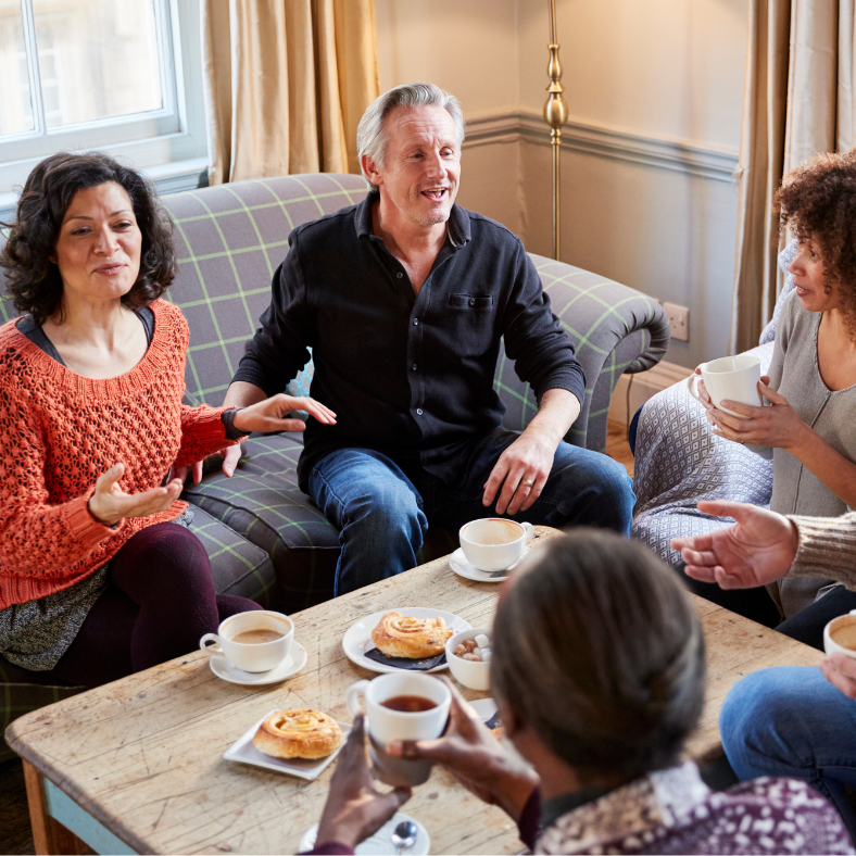 Coffee morning with four adults meeting round a table with cakes and coffee