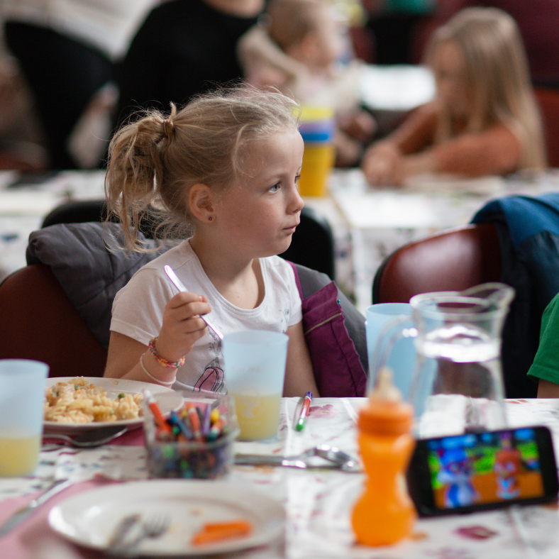 Little girl eating lunch at table with others in background